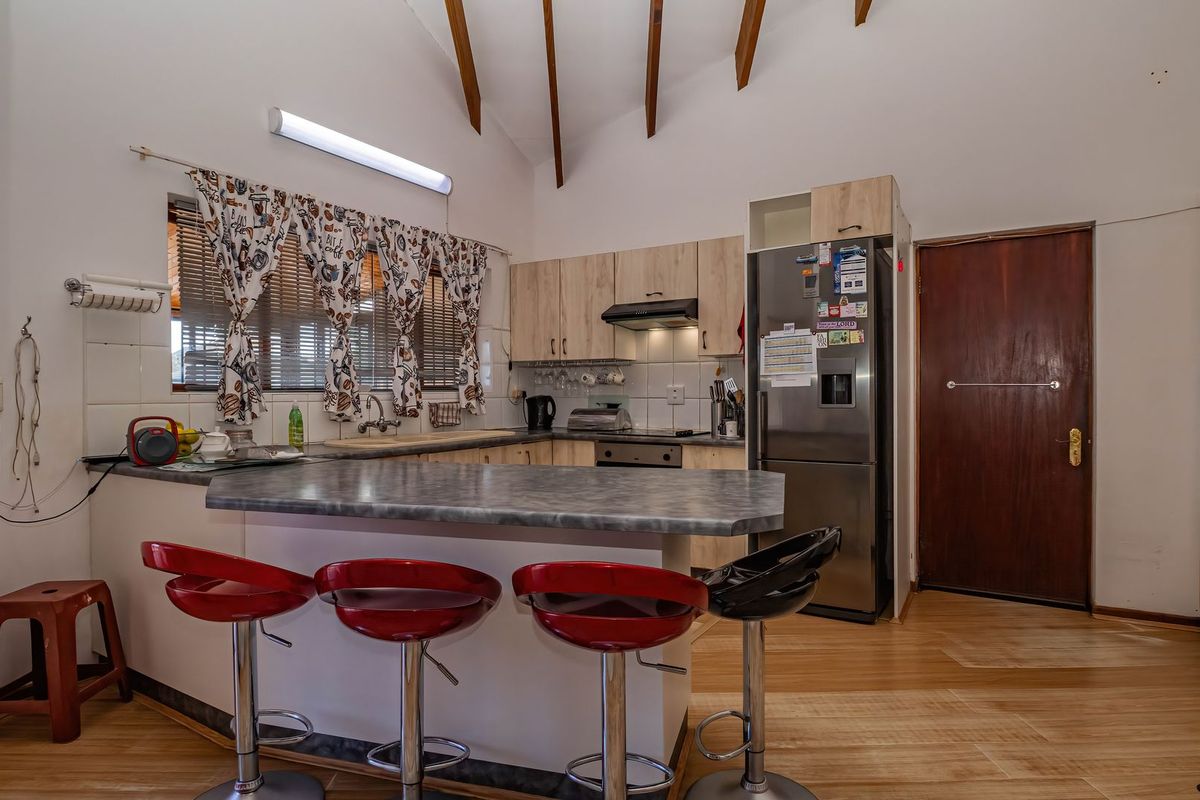 Functional kitchen featuring laminate cabinetry, a breakfast bar, exposed timber ceiling beams, and built-in appliances, offering a practical layout with potential for modern updates.