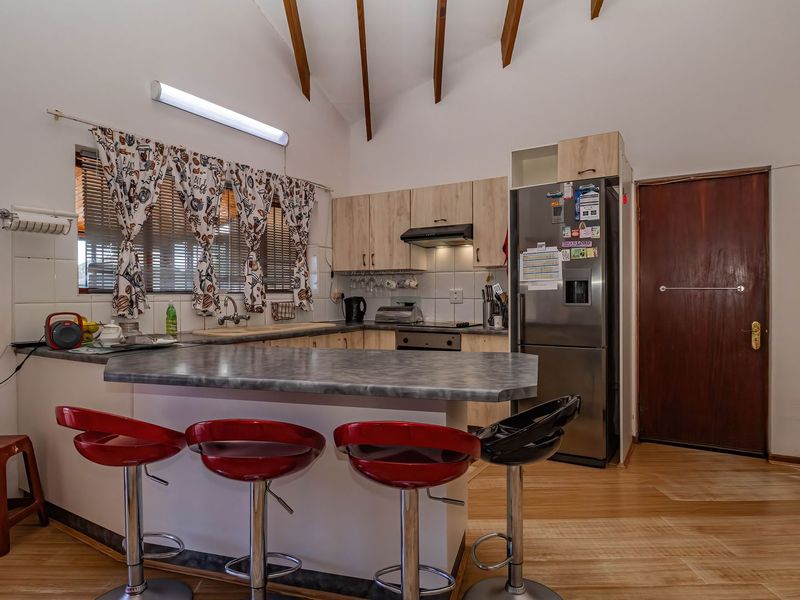Functional kitchen featuring laminate cabinetry, a breakfast bar, exposed timber ceiling beams, and built-in appliances, offering a practical layout with potential for modern updates.