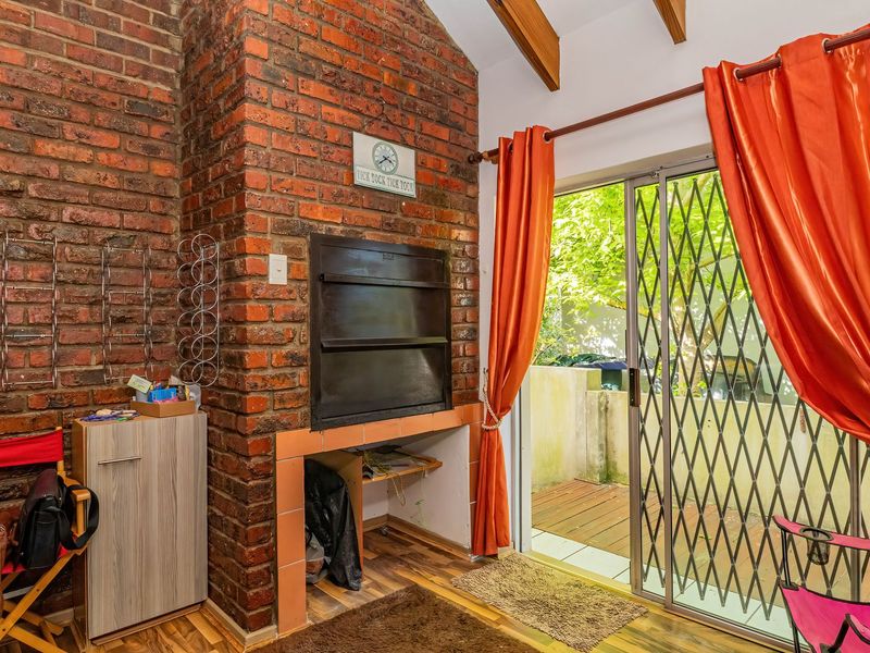 Indoor entertainment area featuring an exposed brick fireplace with a built-in braai, timber ceiling beams, and sliding door access to the outdoor space.