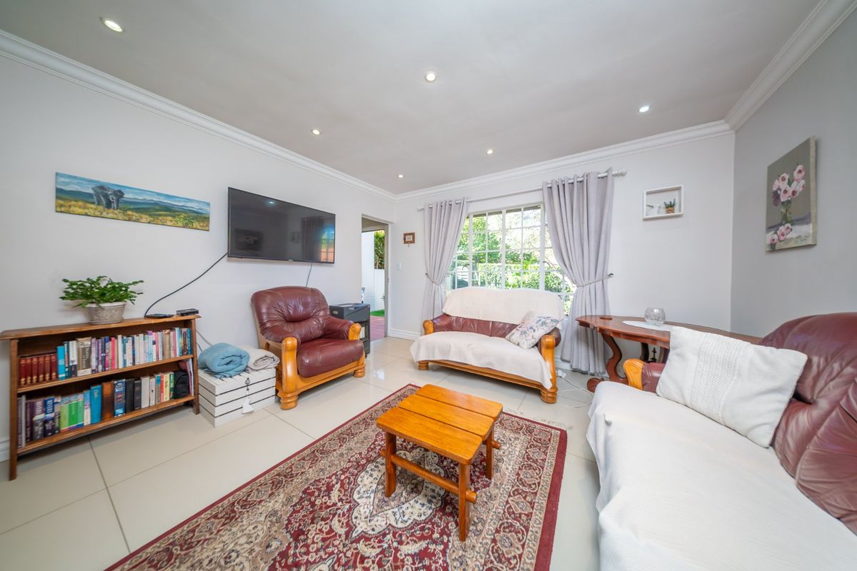 A bright and well-maintained living room featuring tiled flooring, recessed downlighting, and decorative cornicing, offering a comfortable and functional space.