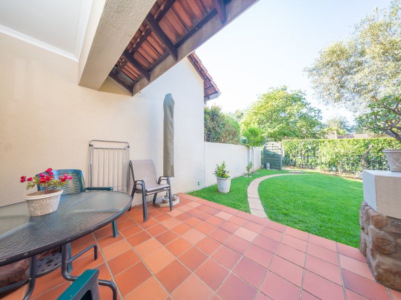 A covered patio with terracotta tiling, featuring a stone-clad pillar and direct access to a private, well-maintained garden area.