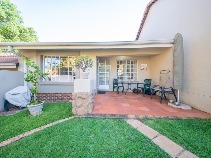 A covered patio area featuring terracotta tiling, a stone-clad pillar, and direct access to the rear garden through multi-pane windows and a glass door.