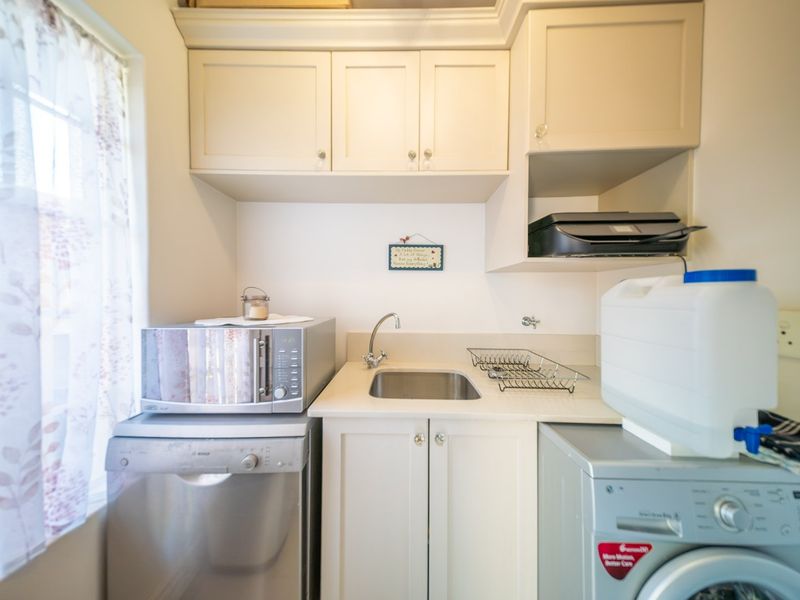 A compact laundry area featuring built-in cabinetry, a stainless steel sink, and dedicated space for appliances.