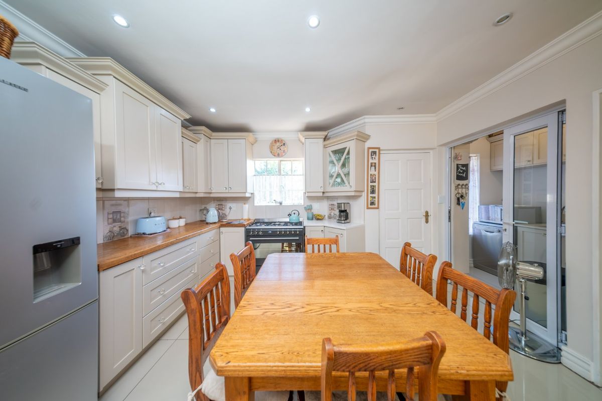 A well-maintained kitchen featuring cream cabinetry, wooden countertops, a gas stove, and recessed lighting, with an adjacent scullery area.