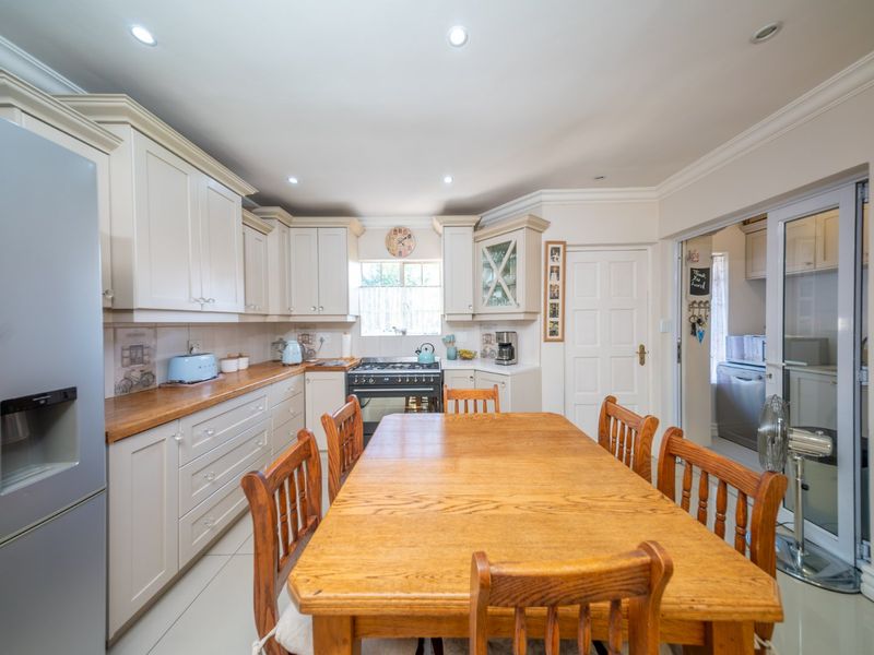 A well-maintained kitchen featuring cream cabinetry, wooden countertops, a gas stove, and recessed lighting, with an adjacent scullery area.