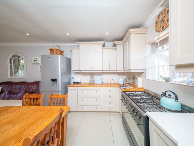 Open-plan kitchen and living area featuring cream cabinetry, wooden countertops, gas hob, and tiled flooring in a well-maintained townhouse setting.