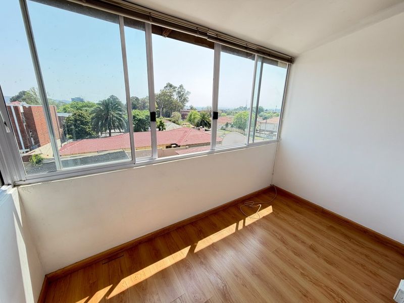 An empty, sunlit enclosed balcony or sunroom featuring large sliding windows with neighbourhood views and durable laminate flooring.