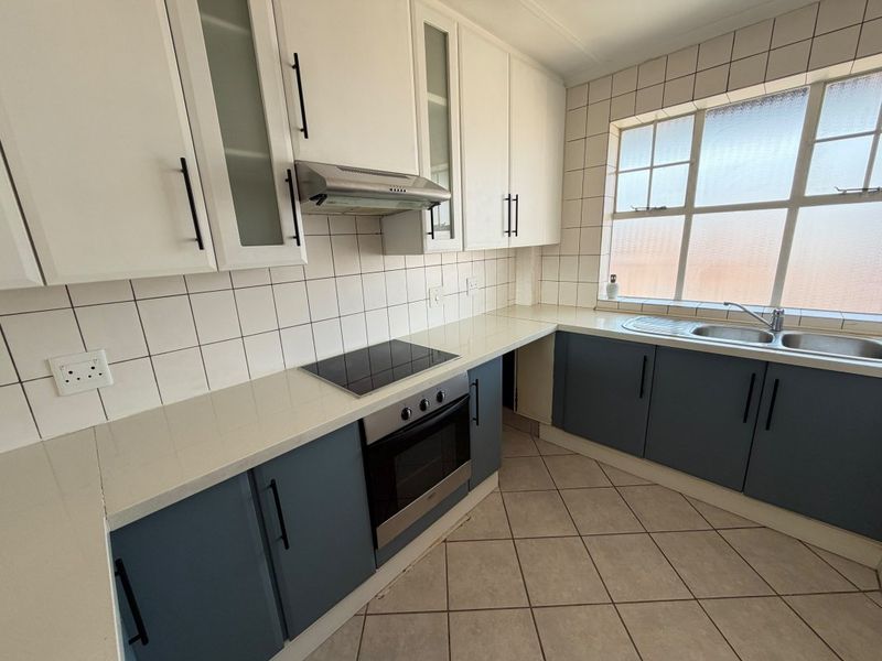 A functional kitchen featuring two-tone cabinetry, quartz countertops, integrated oven and hob, tiled backsplash, and a double sink with natural light.