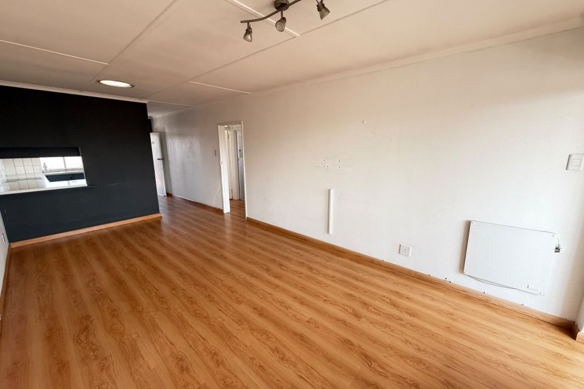 Spacious, empty living area featuring laminate flooring, a wall-mounted electric heater, and a convenient pass-through window connecting to the kitchen space.