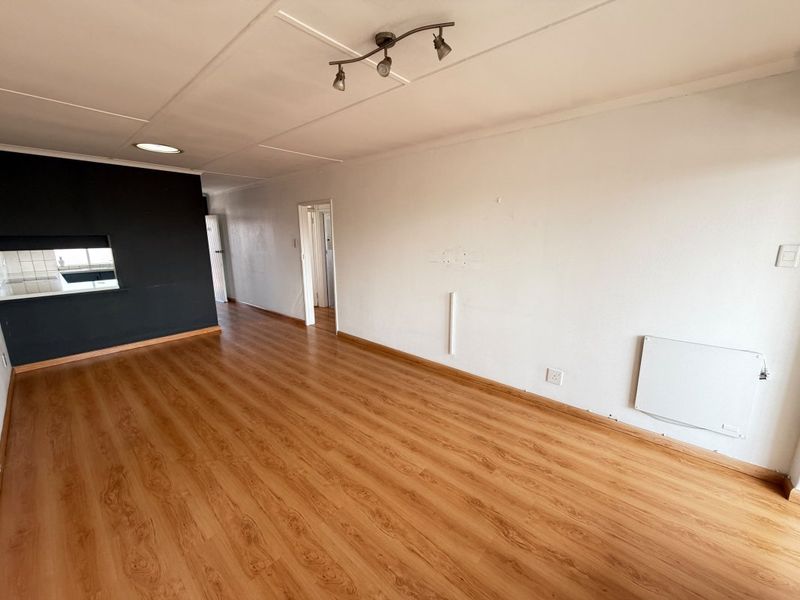 Spacious, empty living area featuring laminate flooring, a wall-mounted electric heater, and a convenient pass-through window connecting to the kitchen space.