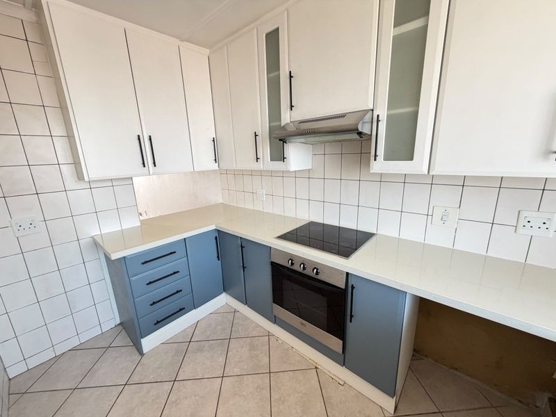 Modern kitchen featuring two-tone cabinetry, stone countertops, integrated electric hob, oven, and extractor fan with a clean tiled backsplash.