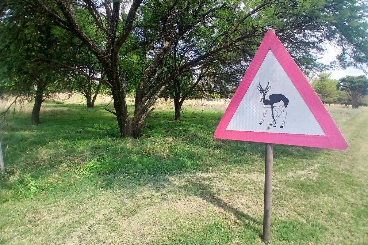 A view of a grassy plot featuring mature trees and a wildlife warning sign, indicating the natural surroundings of the residential land.