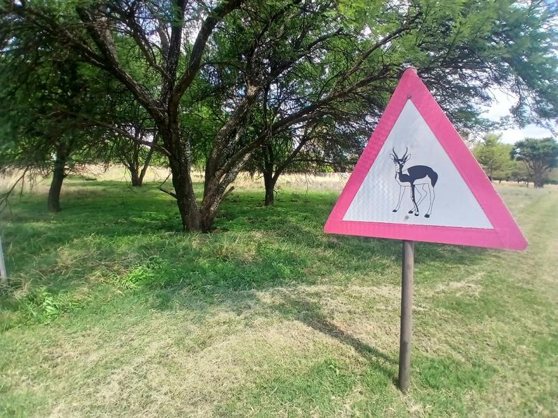 A view of a grassy plot featuring mature trees and a wildlife warning sign, indicating the natural surroundings of the residential land.
