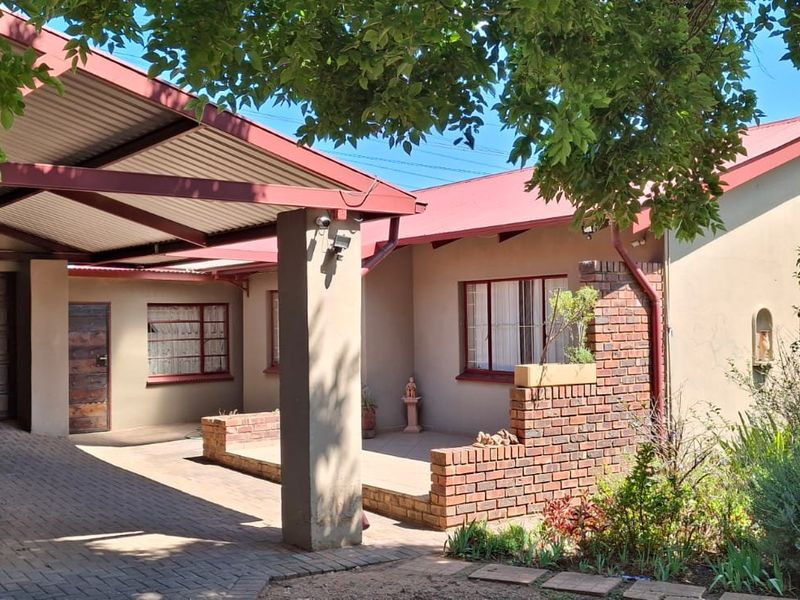 Front elevation of a house featuring a paved driveway, integrated carport, brick boundary wall, and a corrugated metal roof.