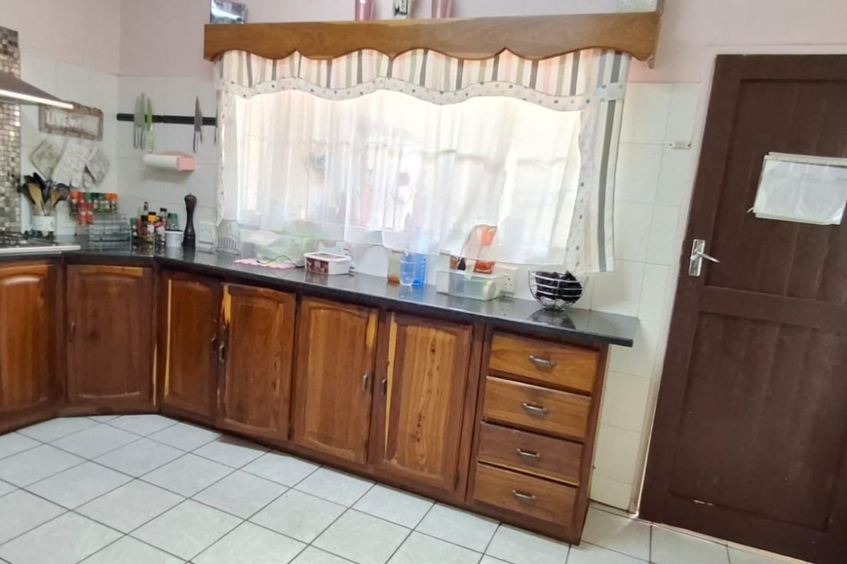 Kitchen featuring wooden cabinetry, granite countertops, gas hob with stainless steel extractor, and tiled flooring. The space offers functional storage and preparation areas.