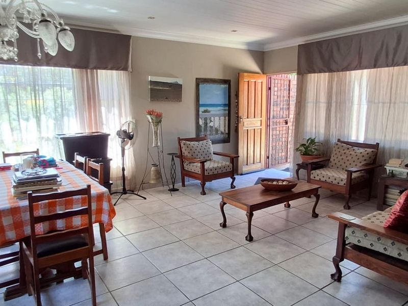 Spacious open-plan living and dining area featuring ceramic floor tiles, a timber panelled ceiling, and direct access to the exterior through a wooden door.