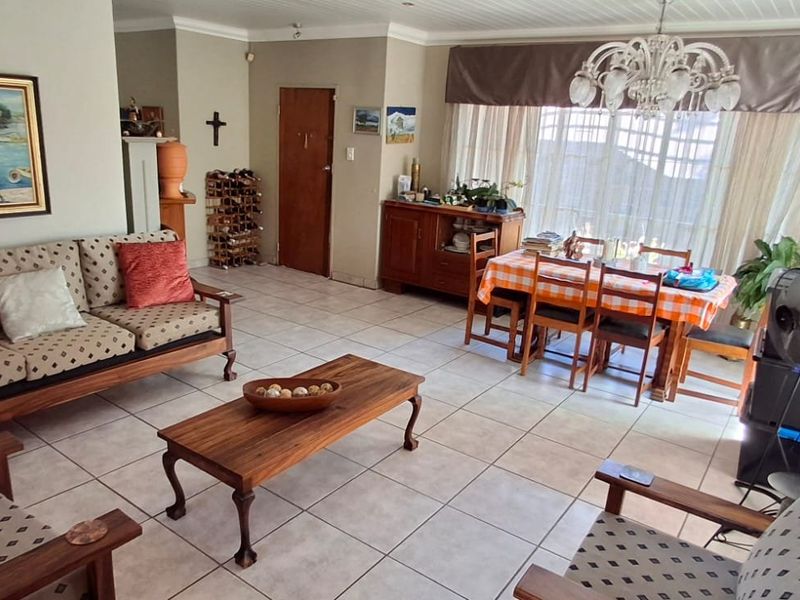 Spacious open-plan living and dining area featuring neutral tiled flooring, large windows for natural light, and classic ceiling cornicing.