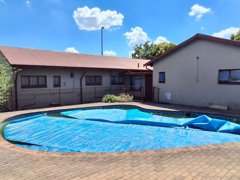 Rear exterior view featuring a swimming pool with a cover, surrounded by paved decking and the rear facade of the house.
