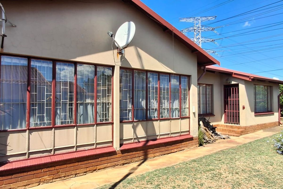 Rear exterior view of the house featuring brick construction, large windows with security bars, and a paved walkway leading to the entrance.