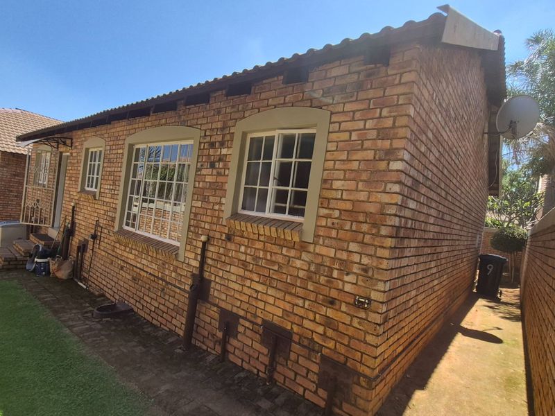 Rear view of the apartment featuring a face brick facade, tiled roof, and paved walkway along the side of the building.