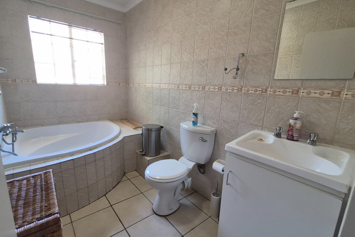 A functional bathroom featuring a built-in corner bathtub, tiled walls and flooring, a vanity basin, and a standard toilet.