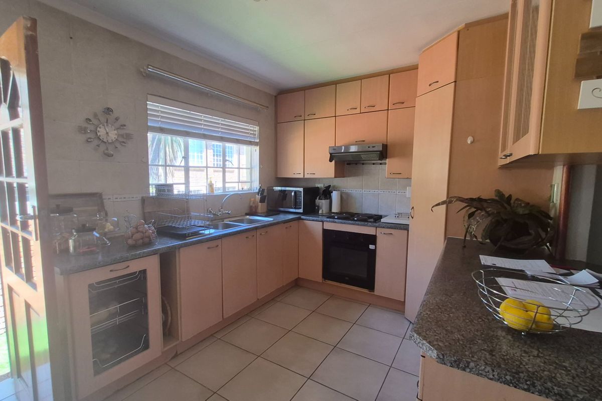 A functional kitchen featuring light wood-tone cabinetry, granite-look countertops, built-in oven, gas hob, and tiled flooring with direct access to the exterior.