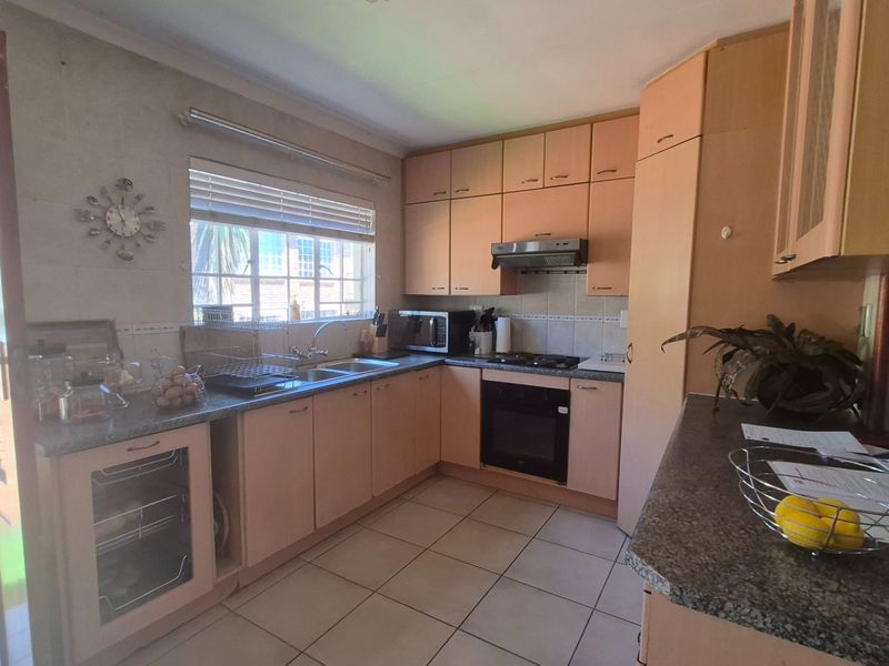 A functional kitchen featuring light wood-tone cabinetry, granite-look countertops, built-in oven, gas hob, and tiled flooring with direct access to the exterior.