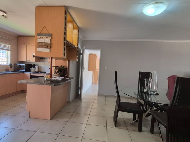 Open-plan living and kitchen area featuring tiled flooring, wooden cabinetry, and a central kitchen island, providing a functional and connected living space.