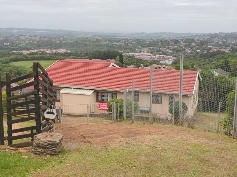 Front exterior view of a residential house featuring a tiled roof, wire mesh perimeter fencing, and a sloping driveway with expansive area views.