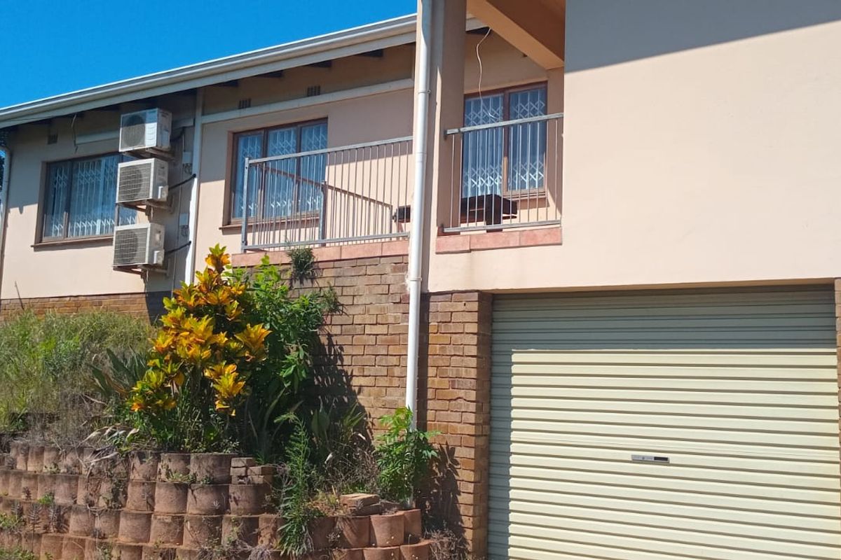 Rear elevation of the house featuring a double garage, a raised balcony with metal railing, and a brick retaining wall with garden area.