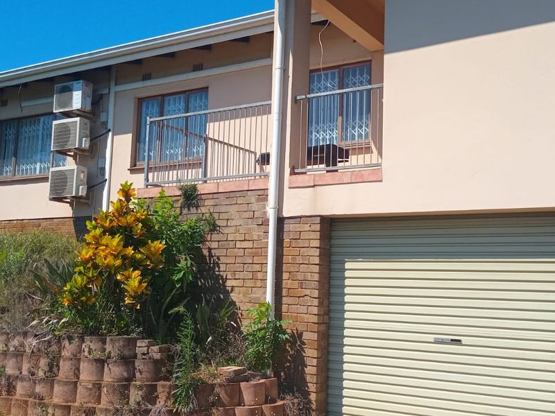 Rear elevation of the house featuring a double garage, a raised balcony with metal railing, and a brick retaining wall with garden area.