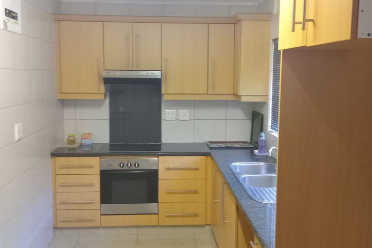 A functional kitchen featuring light wood-finish cabinetry, dark countertops, built-in oven and hob, and tiled splashbacks. The space is currently vacant.