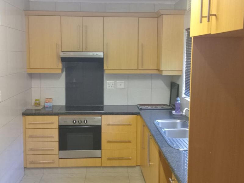 A functional kitchen featuring light wood-finish cabinetry, dark countertops, built-in oven and hob, and tiled splashbacks. The space is currently vacant.