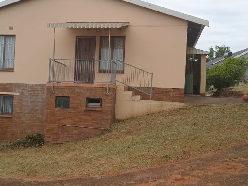 Front exterior view of a single-story house featuring a brick base, metal security railings, and a paved driveway approach.