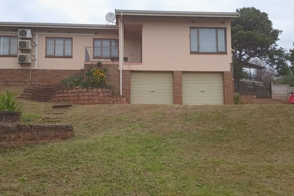 Front view of a single-story house featuring a double garage, brick retaining walls, and an elevated balcony area.