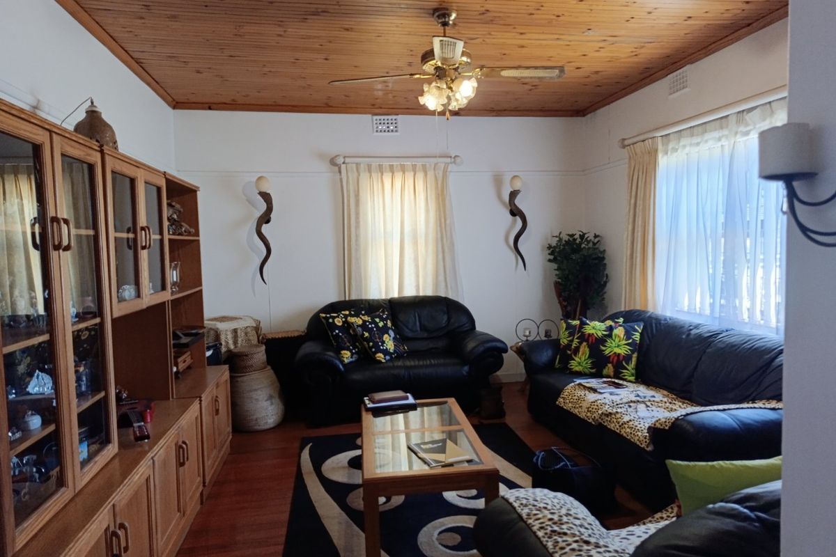 A living room featuring a timber-paneled ceiling, ceiling fan, and timber flooring, complemented by a large built-in wooden wall unit.