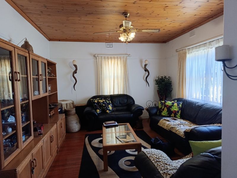 A living room featuring a timber-paneled ceiling, ceiling fan, and timber flooring, complemented by a large built-in wooden wall unit.