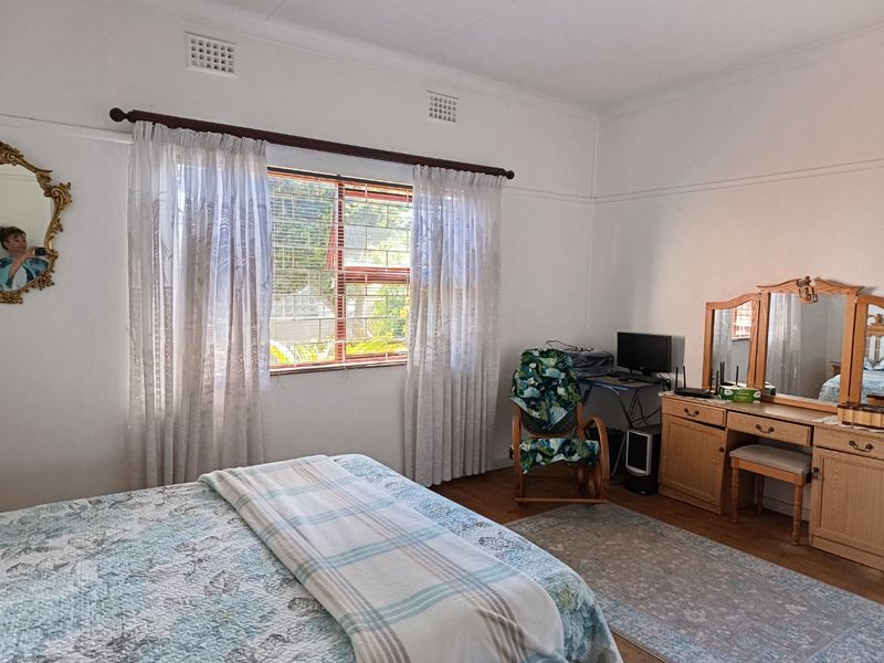A well-lit bedroom featuring timber flooring, classic cornicing, and large windows fitted with security bars.