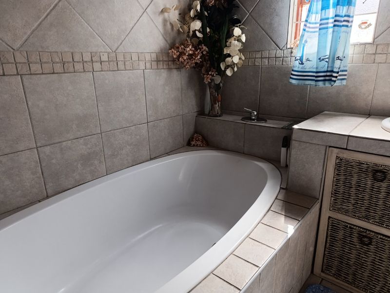 A bathroom featuring a built-in bathtub with neutral ceramic wall tiling and a tiled vanity surround.