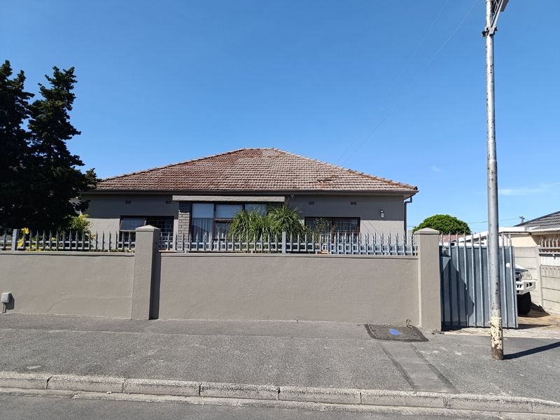 Front exterior view of a single-story house featuring a tiled roof, perimeter wall with security fencing, and a gated driveway entrance.