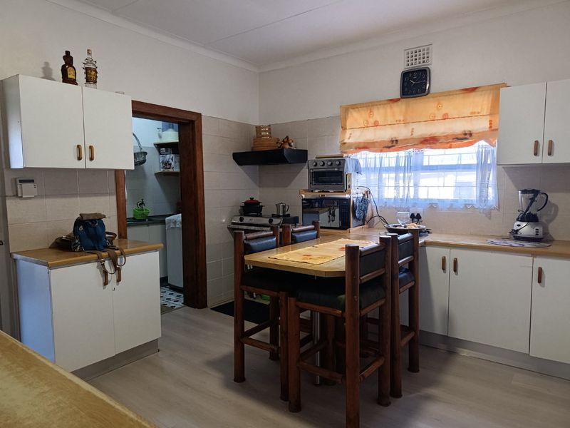 A functional kitchen featuring white cabinetry, laminate countertops, and a tiled backsplash, with an adjacent doorway leading to a secondary utility area.