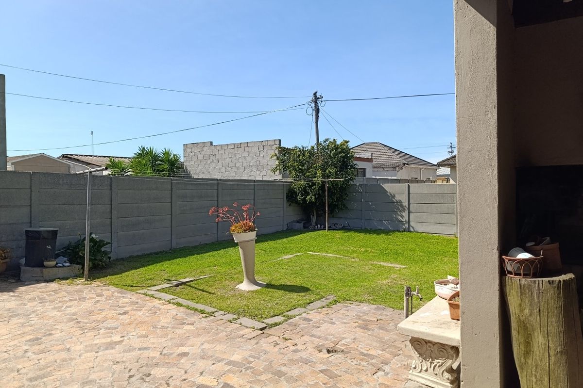 A rear garden featuring a paved patio area, a small lawn, and a precast concrete boundary wall.