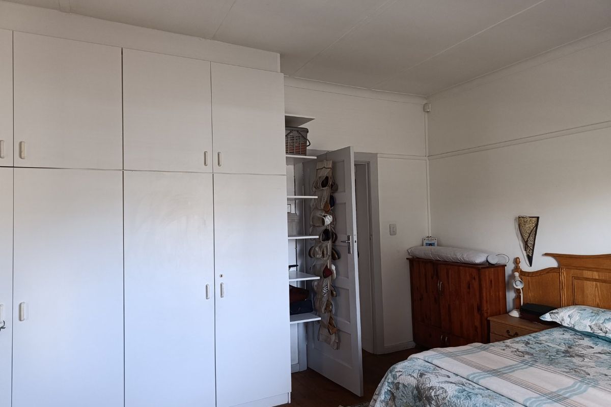A bedroom featuring built-in white cupboards, wooden flooring, and coved ceiling details, offering a functional space with potential for modern updates.