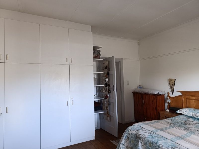 A bedroom featuring built-in white cupboards, wooden flooring, and coved ceiling details, offering a functional space with potential for modern updates.