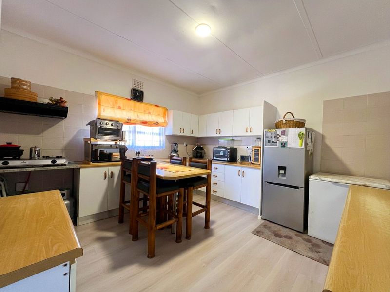 A functional kitchen featuring white cabinetry, laminate countertops, tiled backsplash, and light-toned laminate flooring, offering a practical layout for daily meal preparation.