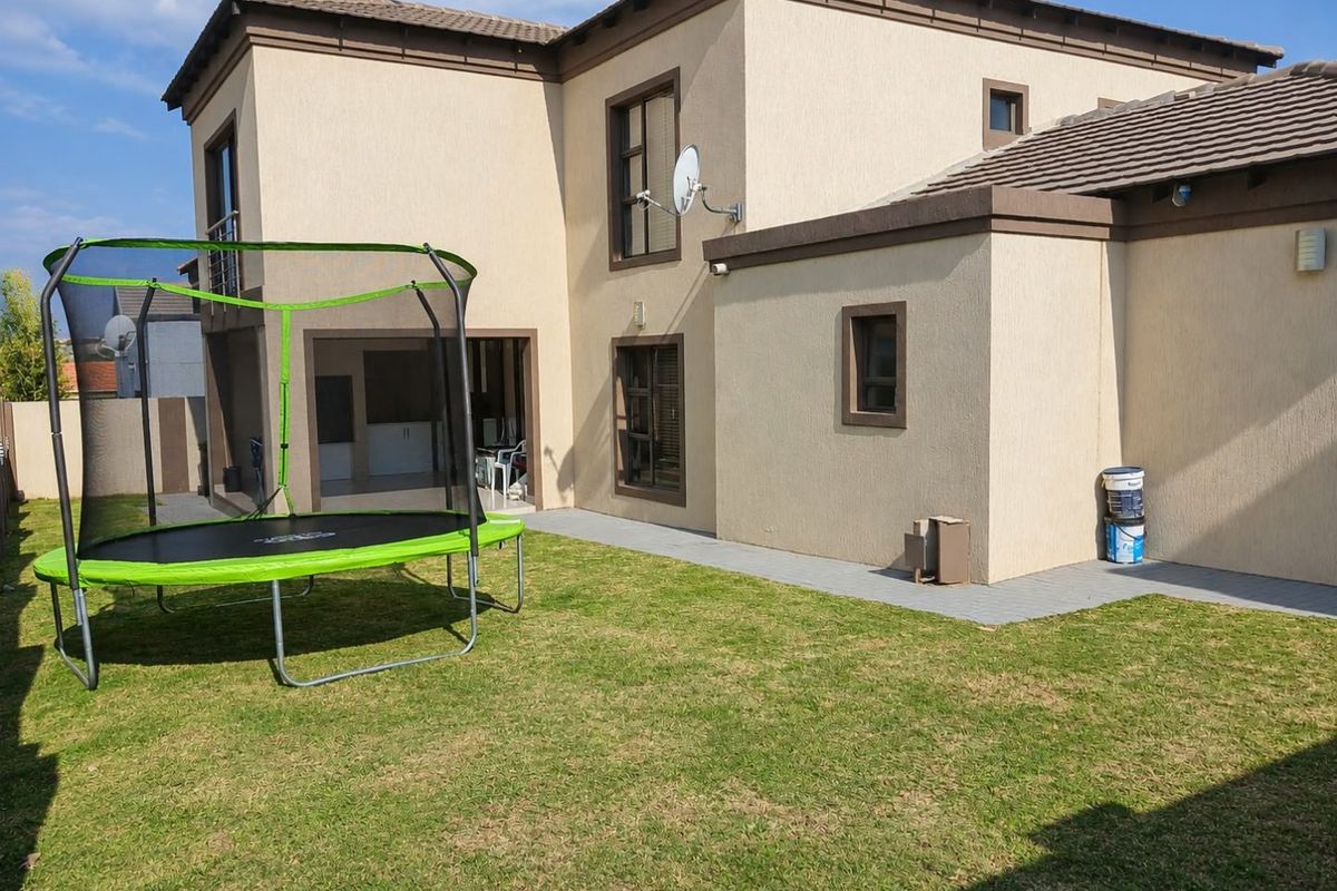 Rear view of a double-storey house featuring a paved walkway, landscaped lawn, and exterior wall lighting.