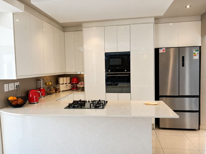 Modern kitchen featuring high-gloss white cabinetry, stone countertops, integrated appliances including a gas hob, oven, and microwave, and sleek tiled flooring.
