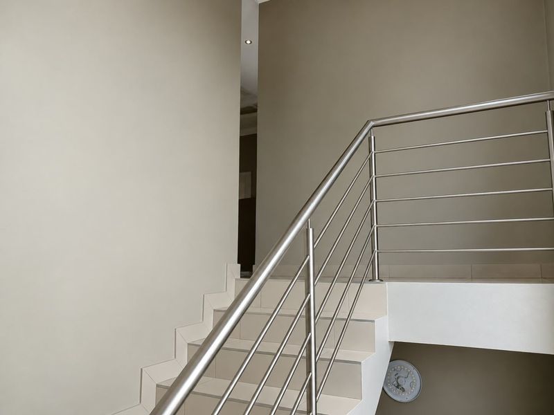 A modern staircase featuring tiled steps and a sleek stainless steel balustrade, providing a clean and contemporary transition between levels.