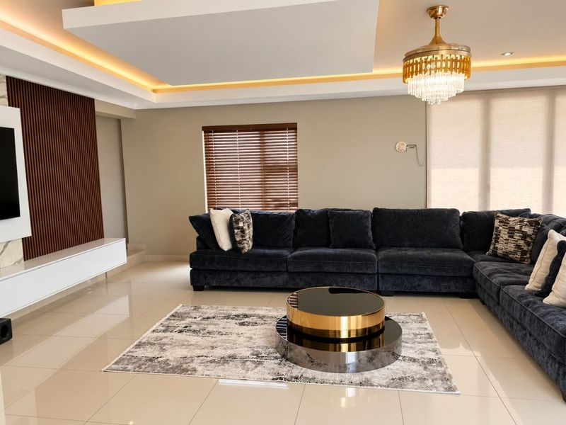Modern living room featuring a recessed ceiling with ambient cove lighting, a crystal chandelier, slatted wood wall accents, and polished porcelain floor tiles.