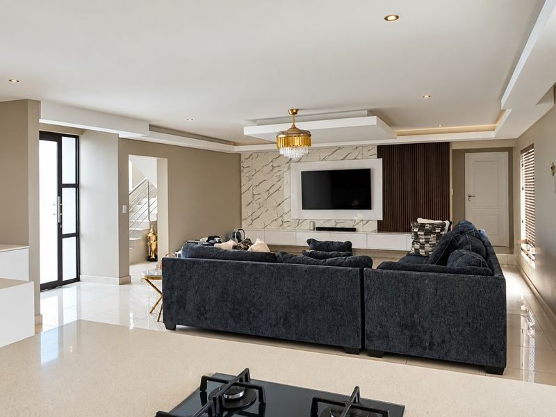 Modern open-plan living area featuring a marble-accented media wall, slatted timber detailing, recessed lighting, and a sleek kitchen island with a built-in gas hob.